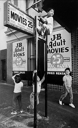 Children playing and climbing parking sign outside adult bookstore Tenderloin San Francisco CA
